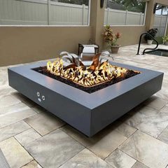 The Outdoor Plus Square Cabo Powder Coated Fire Pit with Yellow Flames and Lotus Flower Burner in Indoor View